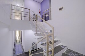 Un intérieur à plusieurs niveaux avec un escalier central, un extincteur fixé au mur et un sol carrelé.
