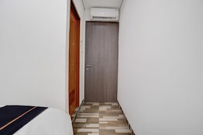 Un couloir étroit avec une porte en bois, un lit recouvert d’une couverture à rayures et un sol à motifs.
