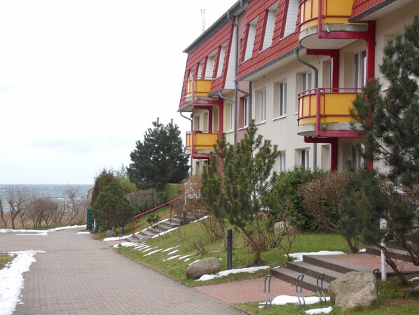 A multi-story building with balconies, a paved pathway, and a view of the sea. - Apartment complex Dünengarten 1st floor for 2 persons (Kühlungsborn)
