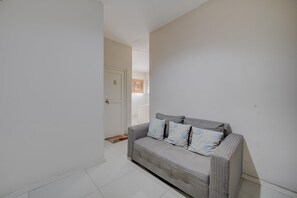 Un couloir avec un canapé et des coussins à rayures, une porte blanche et un tableau encadré au mur.