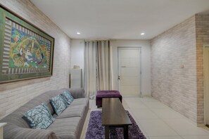 Un salon avec un canapé, une table basse, un tapis violet, une porte et un mur orné d’un tableau encadré.