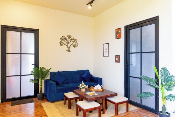 Une pièce avec un canapé bleu, une table basse en bois, une plante en pot et une porte-fenêtre coulissante.