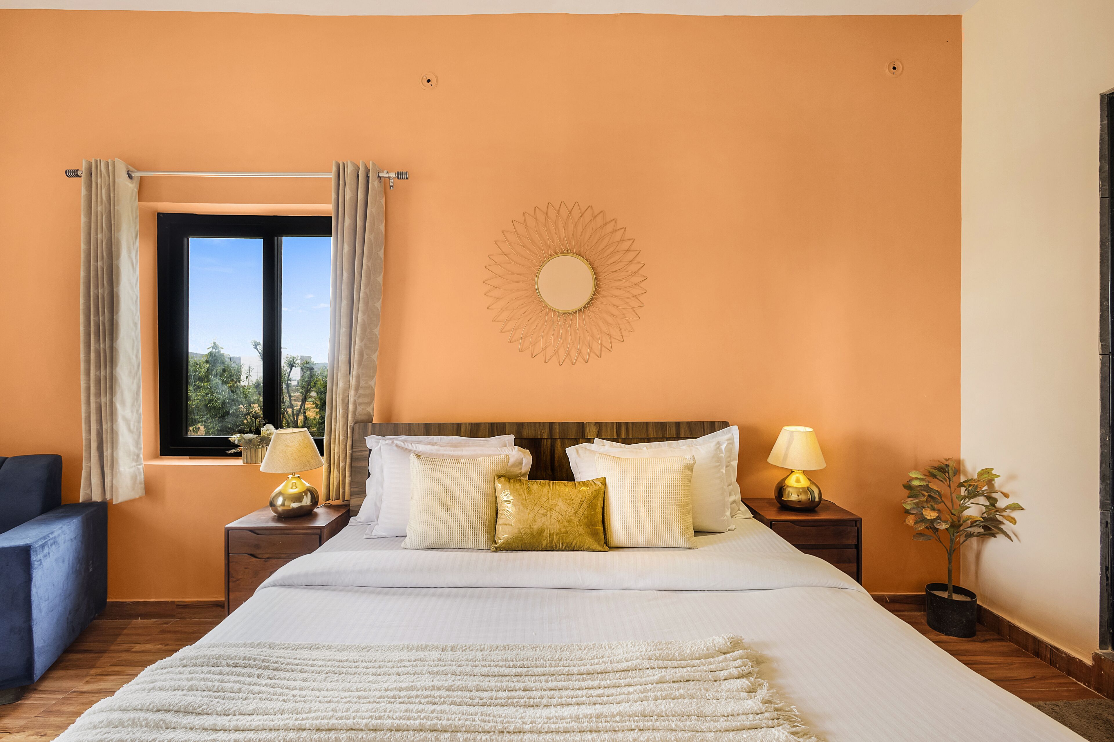 Een slaapkamer met een bed, twee nachtkastjes, een raam met gordijnen, een zonversiering aan de muur en een kamerplant in een pot.