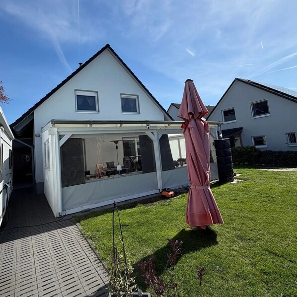 A house with a covered patio area, a lawn, and a large umbrella. - Accommodation with 1-3 Private Rooms, No Kitchen, with Wi-Fi (Laatzen)