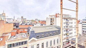 En stadsbild med olika byggnader, inklusive en framträdande vit byggnad med en balkong och en metallkonstruktion i förgrunden.