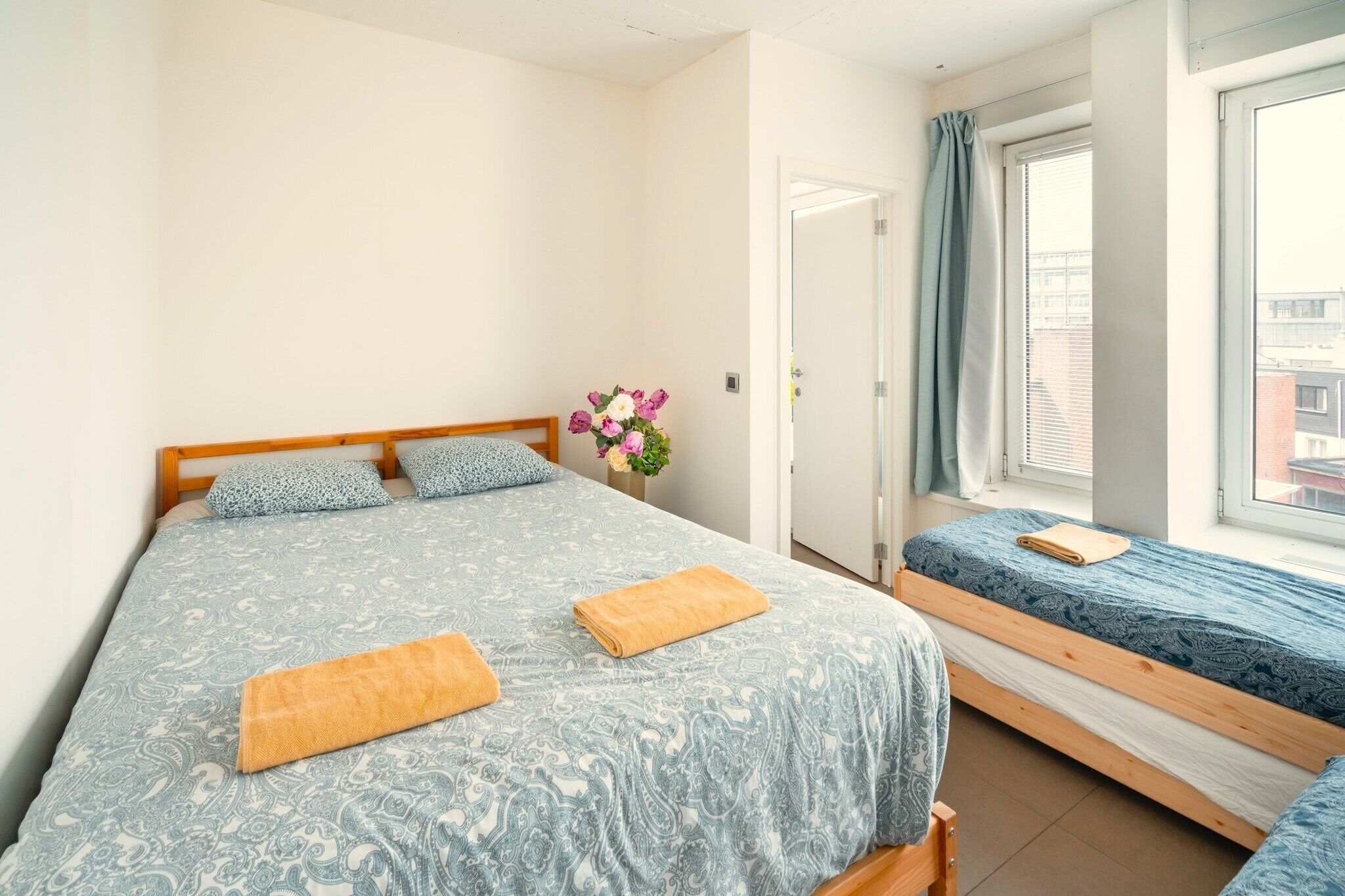 A bedroom with a large bed and a smaller bed, both with patterned bedding, a wooden headboard, and a window with curtains.