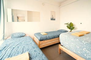 A room with three single beds, each with a blue patterned bedspread and a wooden frame. There is a mirror on the wall, a small plant, and a picture frame. - Centrally Located Antwerp Stay for 10 (Antwerp)