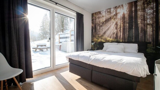 Ein Schlafzimmer mit Bett, Stuhl, einer Glaswand und Wandgestaltung zum Thema Wald.