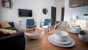 Ett modernt vardagsrum med en soffa, två fåtöljer, ett soffbord och ett matbord med vita tallrikar och ett glas.