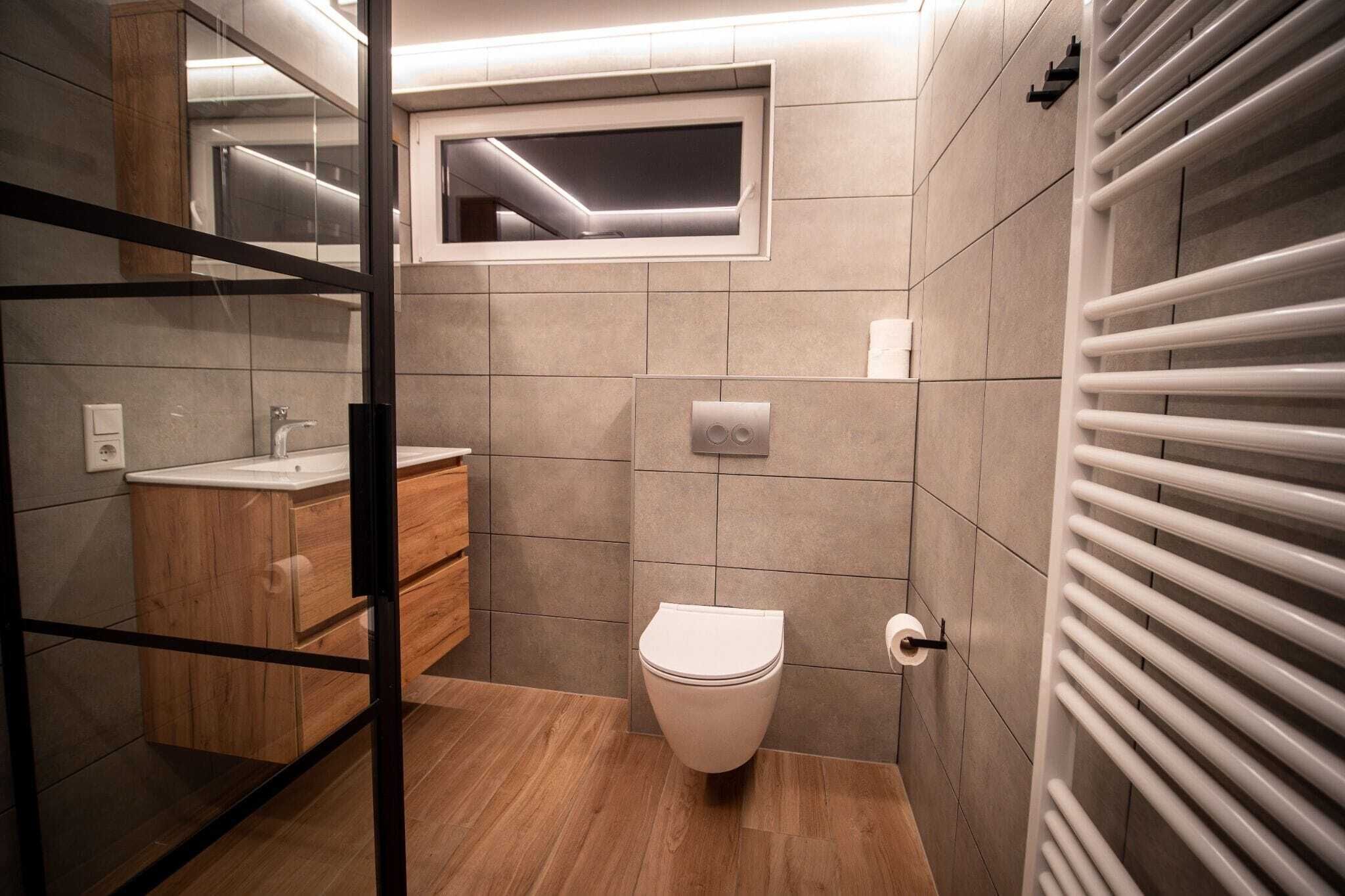 Een moderne badkamer met toilet, wastafel en een raam boven het toilet.