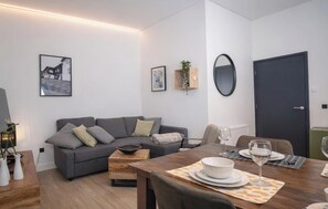 A modern living room with a grey sofa, a wooden coffee table, and a dining table set for two with plates and glasses. - Winterberg Apartment an Lift und Piste (Winterberg)