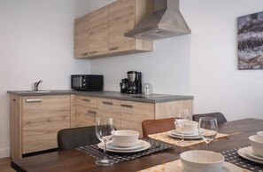 A modern kitchen with wooden cabinets, a microwave, a coffee maker, and a dining area with a table set for two. - Winterberg Apartment an Lift und Piste (Winterberg)