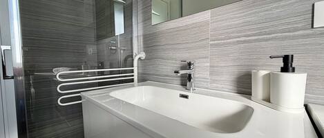 A modern bathroom with a large white sink, a glass shower enclosure, and a mirror.