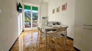 A dining area with a table, chairs, a hanging light fixture, and a view through a door. - Schiappacasse 11 (Rapallo)
