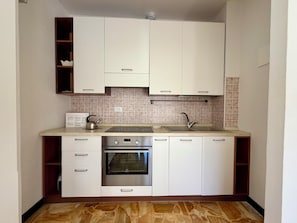 Una cocina compacta con armarios blancos, horno empotrado, pileta de acero inoxidable y salpicadero de azulejos.