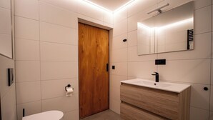 Ein modernes Badezimmer mit Holztür, weißen Fliesen, einem weißen Waschbecken und einem Spiegel.
