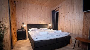 Ein Schlafzimmer mit einer Holzwand, einem Bett mit weißer Bettwäsche, einem Nachttisch mit Lampe und einer Bank.