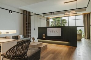A modern interior with a sofa, a chair, a desk, a large window, and a wall-mounted sign. - Zins Luxury Apartments (Durrës)