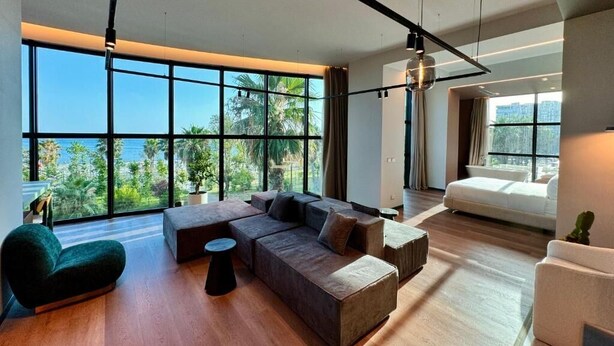 A modern living room with large windows, a sectional sofa, a round coffee table, and a white couch. - Zins Luxury Apartments (Durrës)