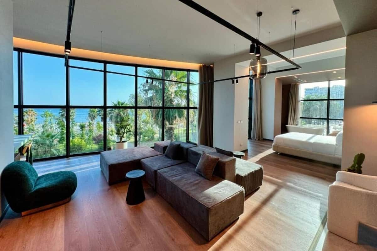 Una sala de estar moderna con ventanas amplias, un sofá modular, una mesa de centro redonda y un sofá blanco.