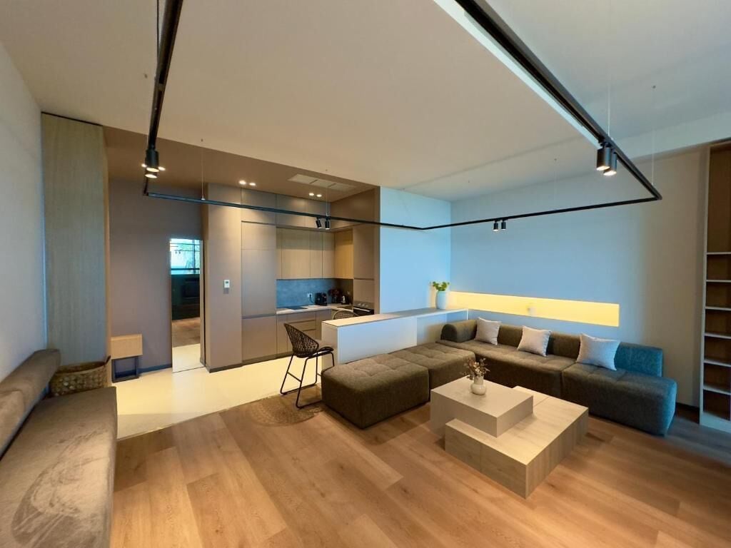 Ein modernes Wohnzimmer mit einem Ecksofa, einem Couchtisch und einer Küchenzeile im Hintergrund.