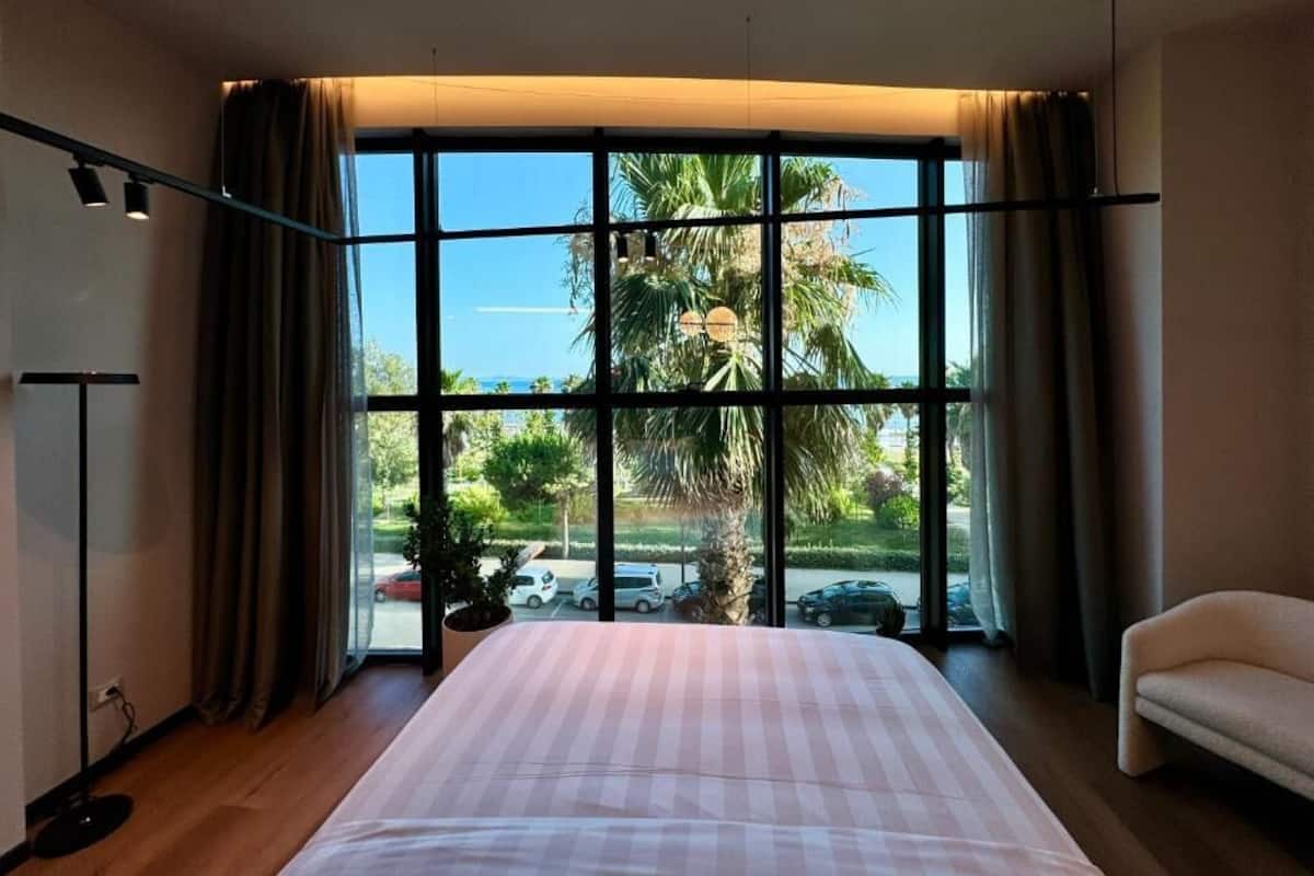 Una habitación de hotel con un ventanal grande, una cama, una silla y una planta.