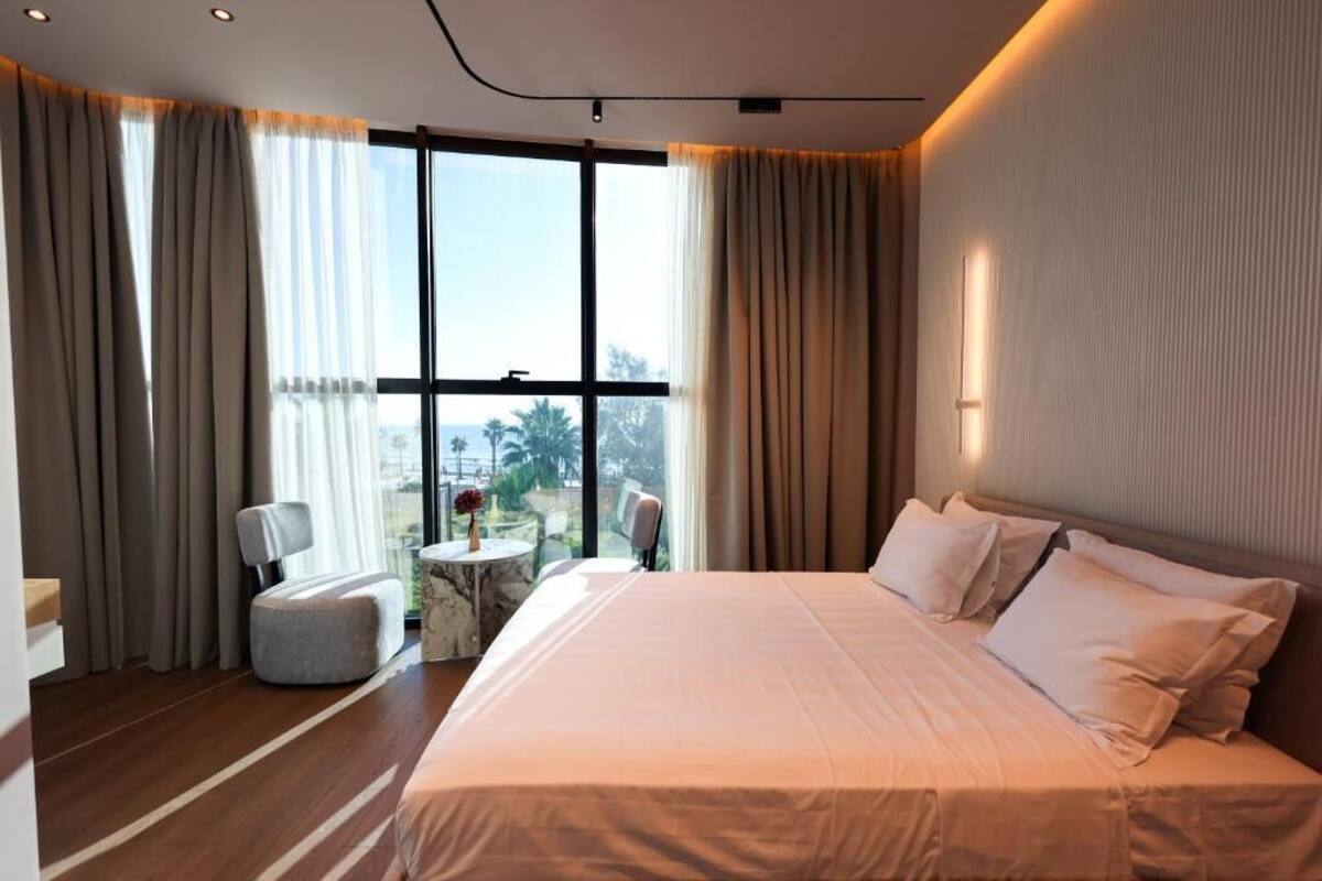 Una habitación de hotel con una cama grande, una mesa redonda, dos sillas y vistas al exterior a través de amplios ventanales.