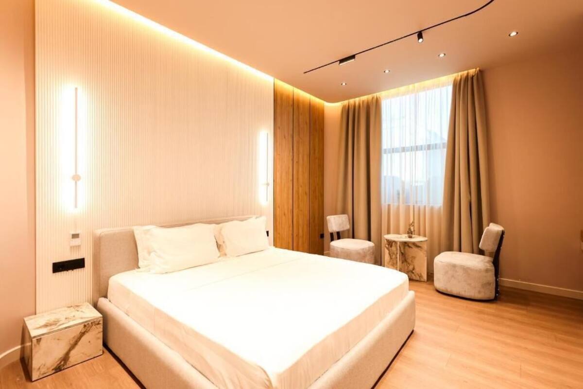 Una habitación de hotel moderna con una cama grande, una mesita redonda pequeña, una silla y una ventana con cortinas.