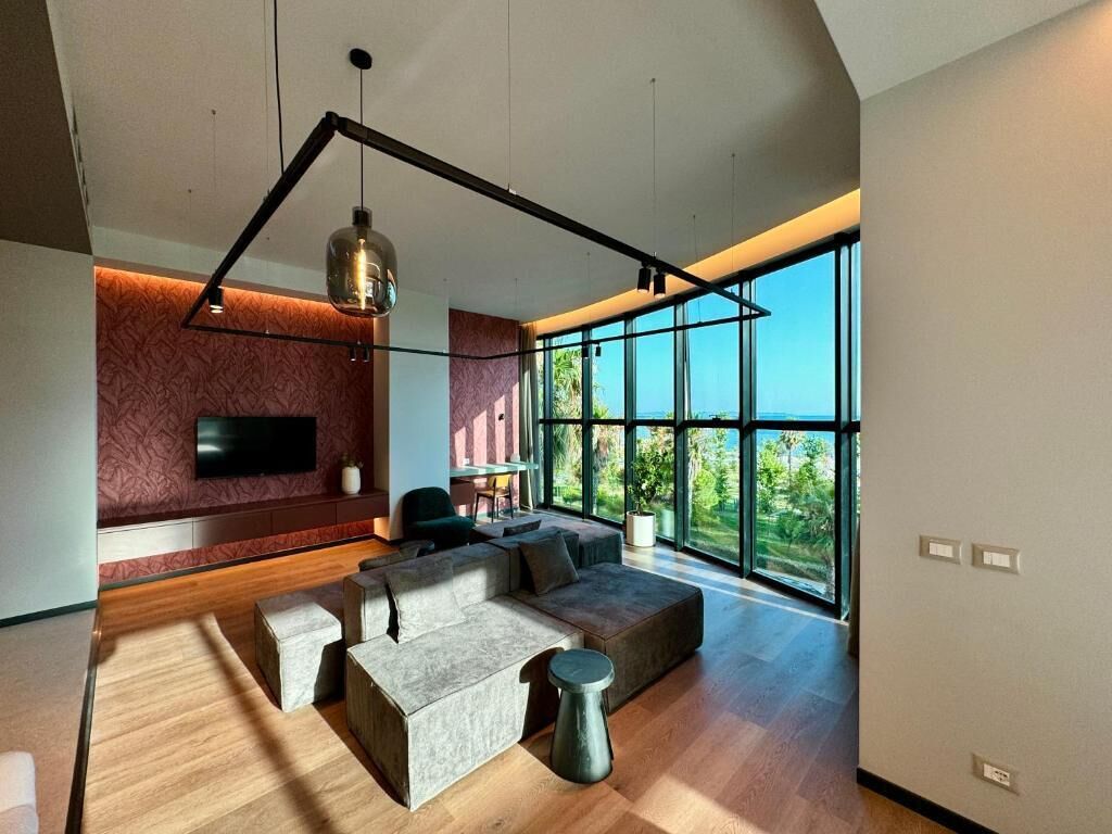 A modern living room with a large window, a sofa, a coffee table, and a TV mounted on the wall.