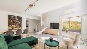 Un salon moderne avec un canapé vert, une table à manger avec des chaises, un escalier, un téléviseur et un balcon avec vue.