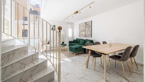 Un intérieur moderne avec un escalier, un coin repas comprenant une table et des chaises en bois, un canapé vert et un tableau au mur.