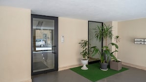 A hotel lobby with a glass door, potted plants, a green mat, and a wall-mounted information board. - Levante Eight Sea View Holiday Home with Sea View, Wi-Fi, and Air Conditioning (Bari)