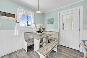 A room with a bench seating area, a table with a vase of flowers, a door with a window, and a wall-mounted shelf with baskets. - Sandy Toes Hideaway- Multi Family! (Panama City)