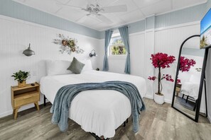 Ein Schlafzimmer mit Bett, Nachttisch, Lampe, Wanddekoration, Fenster, Vorhängen und einem Spiegel.