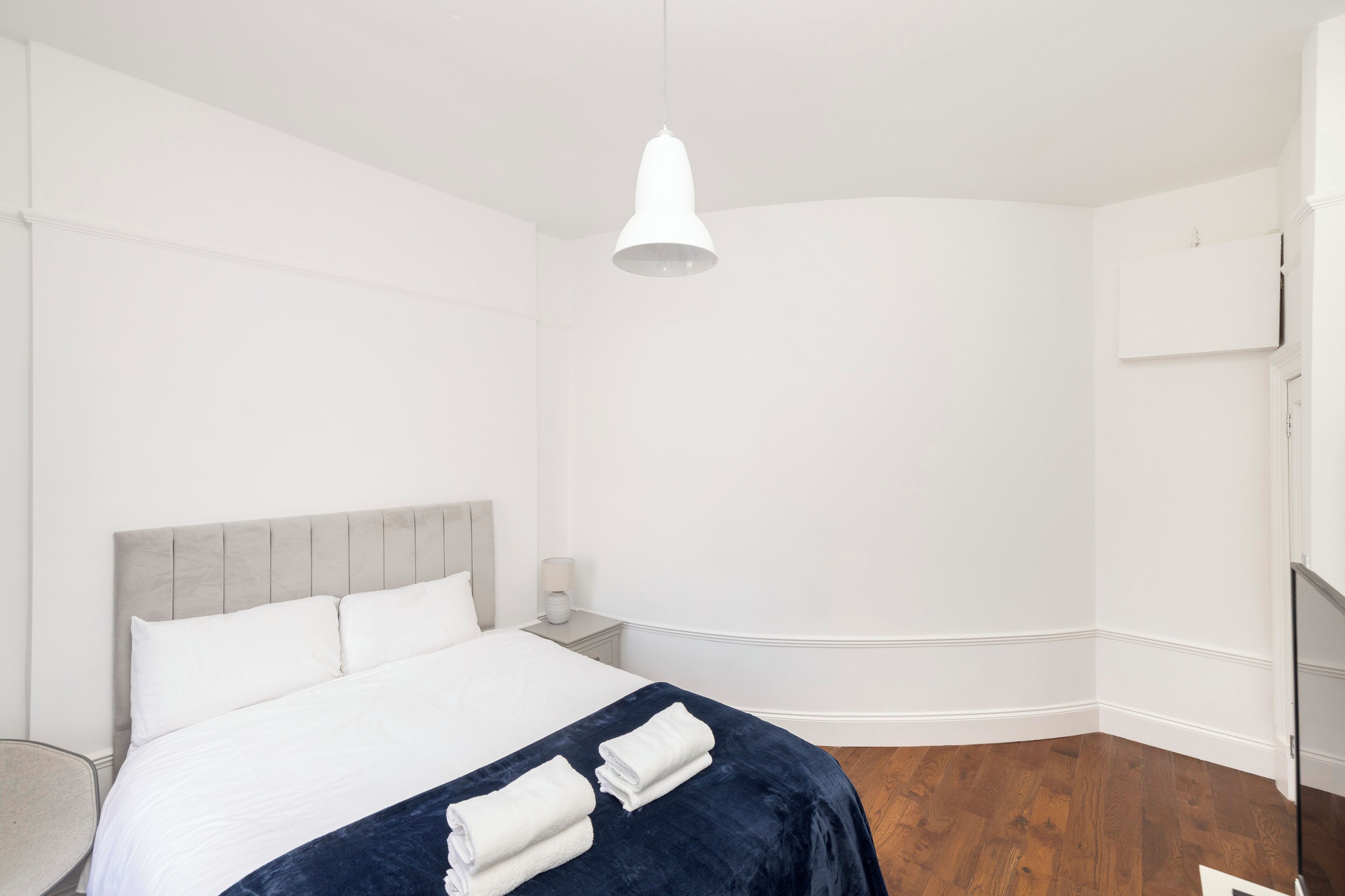 A hotel room with a bed, a bedside table, a lamp, and a white pendant light.