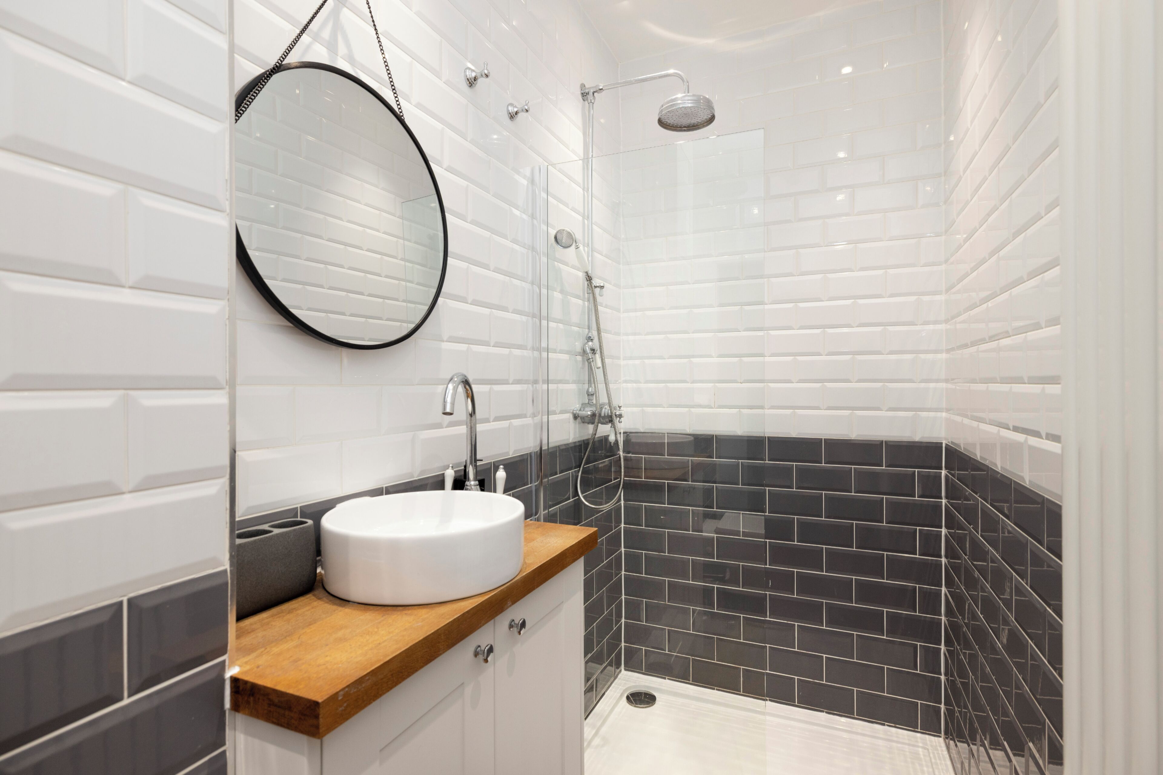 A modern bathroom with a round mirror, a sink, and a shower area.