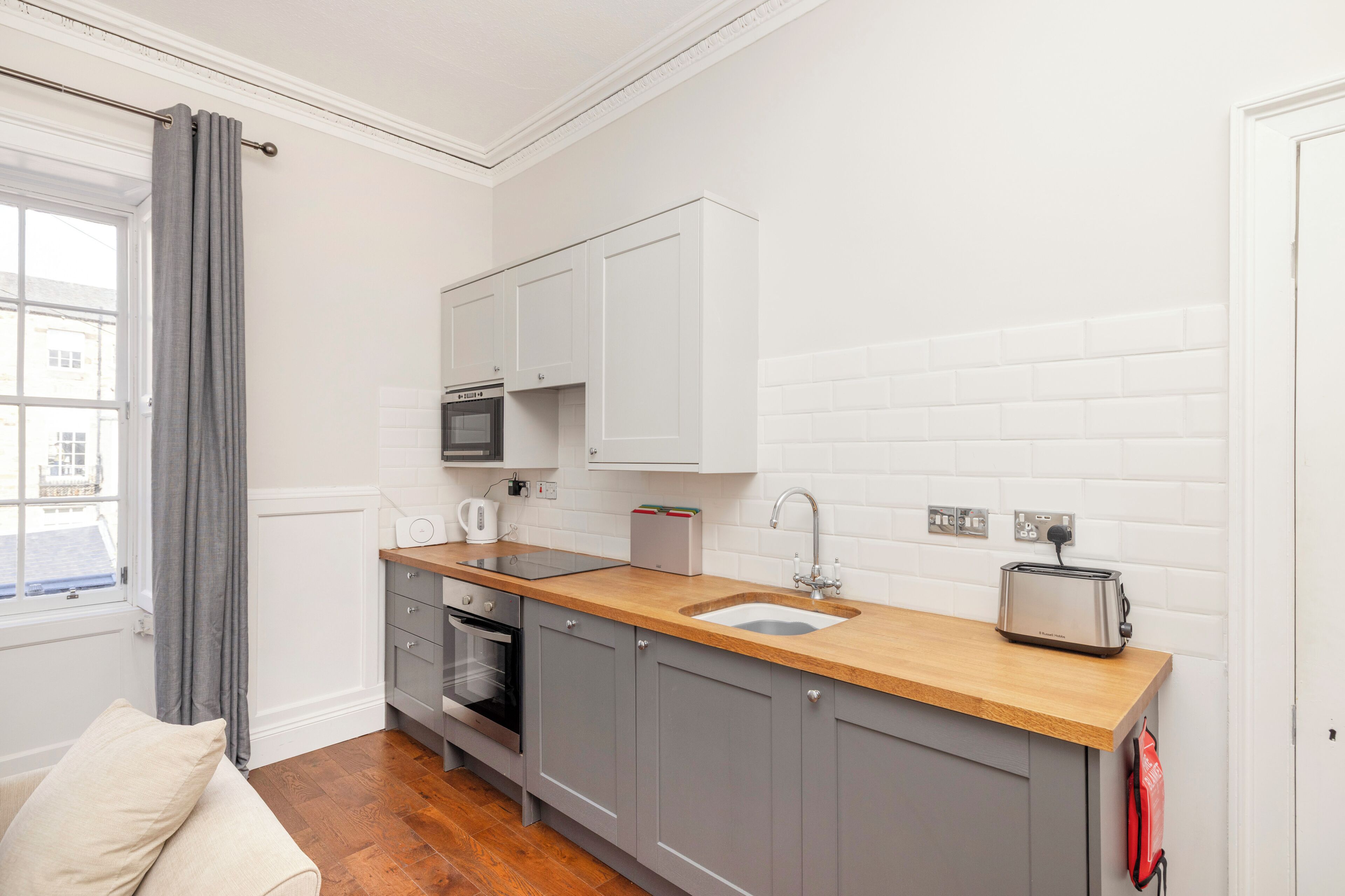 Une cuisine compacte dotée d’un plan de travail en bois, d’un four encastré, d’un évier et de placards blancs.
