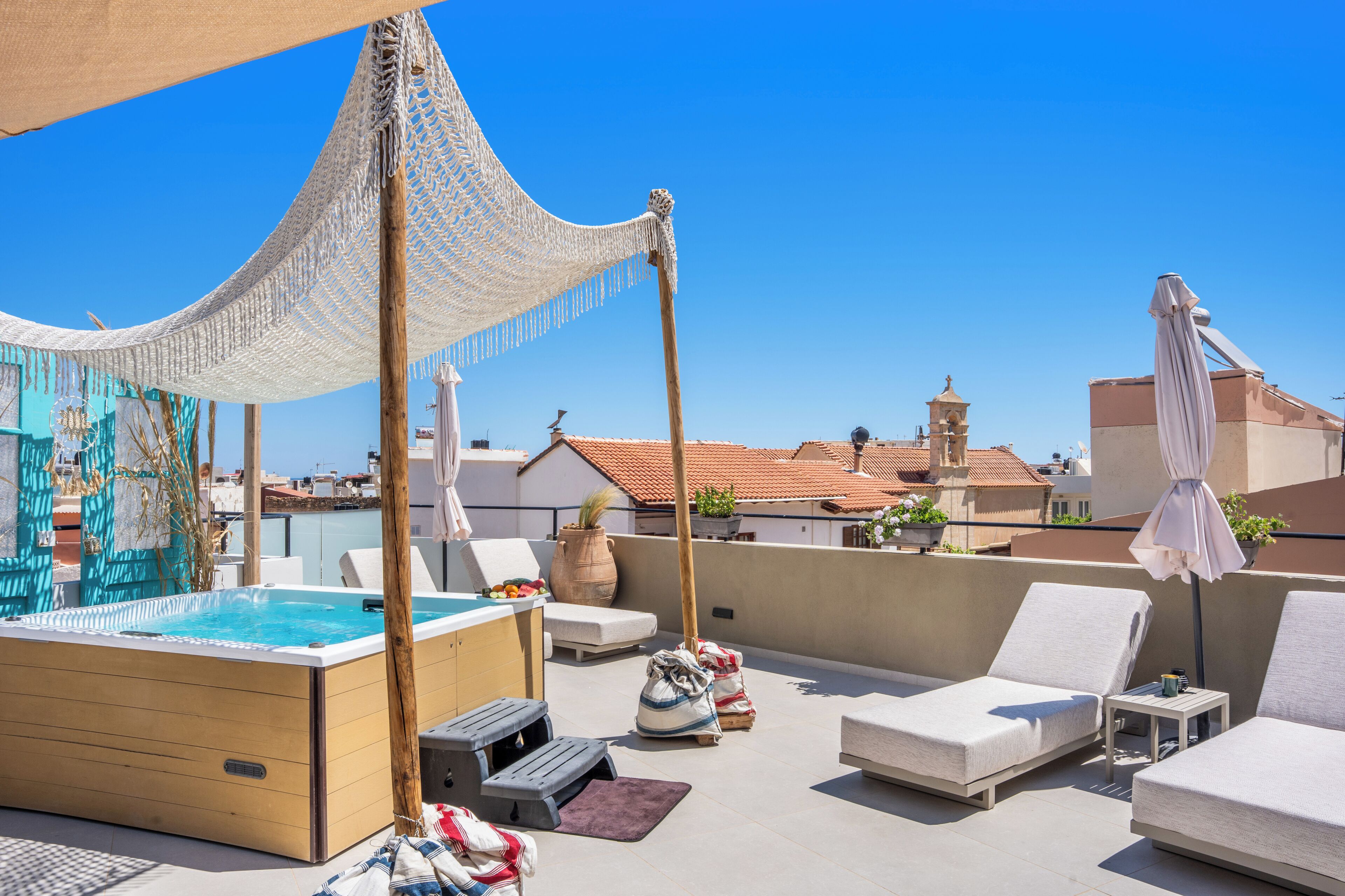 Un área de piscina en la azotea con sillones de descanso, un jacuzzi y una pérgola con mosquitera.