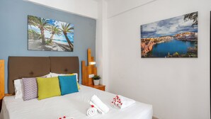A hotel room with a bed, pillows, a nightstand, a lamp, and two wall-mounted paintings. - malia boutique studios (Malia)