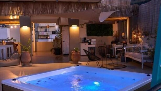 A hot tub in a covered outdoor area with seating and a kitchen in the background. - malia boutique studios (Malia)