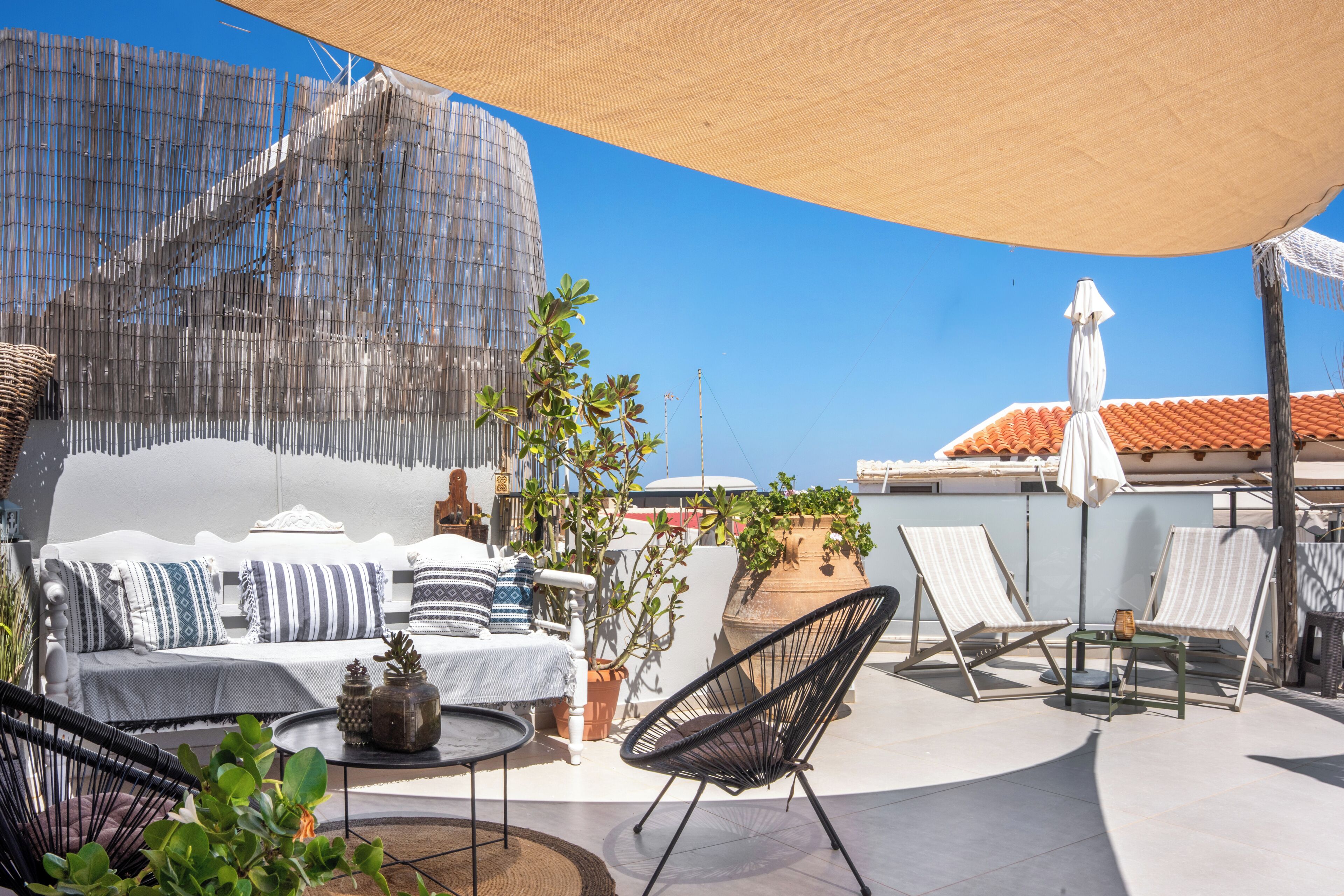 A rooftop terrace with a seating area, including a sofa and chairs, under a large shade structure.
