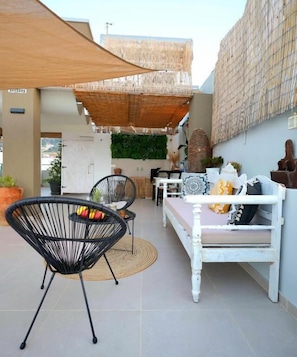 Eine Terrasse im Freien mit einem weißen Sofa, schwarzen Stühlen und einem gewebten Sonnenschutz.
