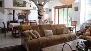 Un salon chaleureux avec un canapé en cuir marron, une table à manger avec des chaises, une cheminée et une grande fenêtre.