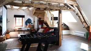 Une pièce de style loft avec des poutres apparentes, une table de baby-foot, un canapé et un escalier.