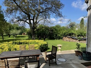Eine Terrasse mit Tisch und Stühlen, ein großer Baum und eine Steinmauer im Hintergrund.