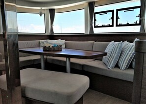 A cozy RV interior with a dining table, cushioned seating, and large windows. - Sun-Kissed Sailing Adventure in the Saronic Islands (Laurium)