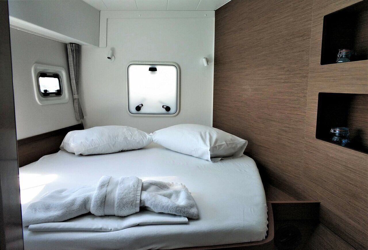 Een bed met witte lakens, een raam met gordijnen en een klein plankje met een potje.