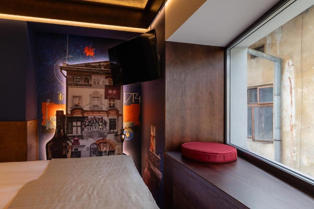 A hotel room with a bed, a red cushion, a television, and a wall mural.