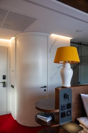 A hotel room with a white door, a round table with a remote control, a yellow lamp, and a control panel with buttons. - FEST hotel. Rynok Square (Lviv)