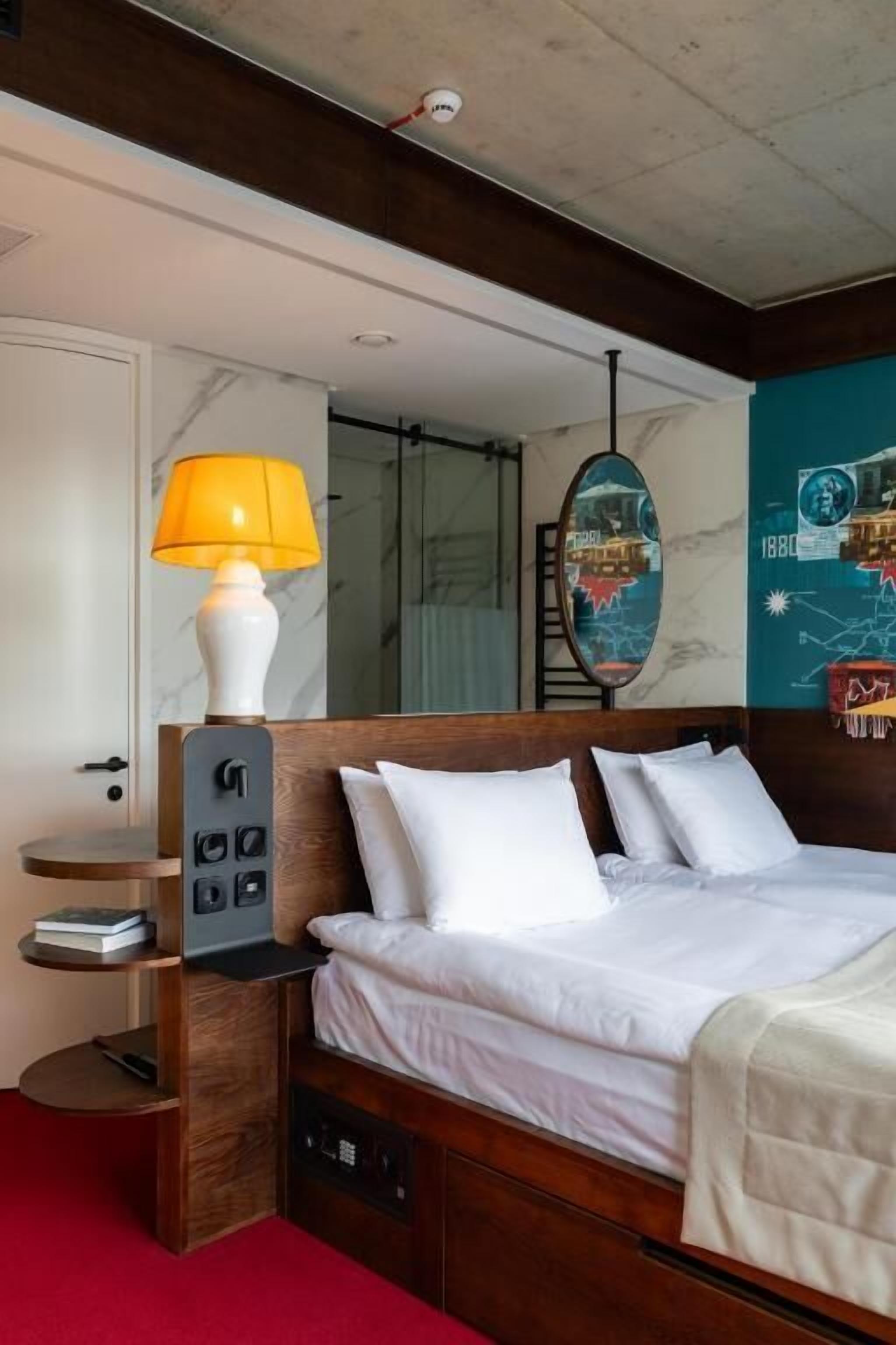 Una habitación de hotel con una cama de madera, una mesita de noche con lámpara, un espejo y una pared con un mapa.